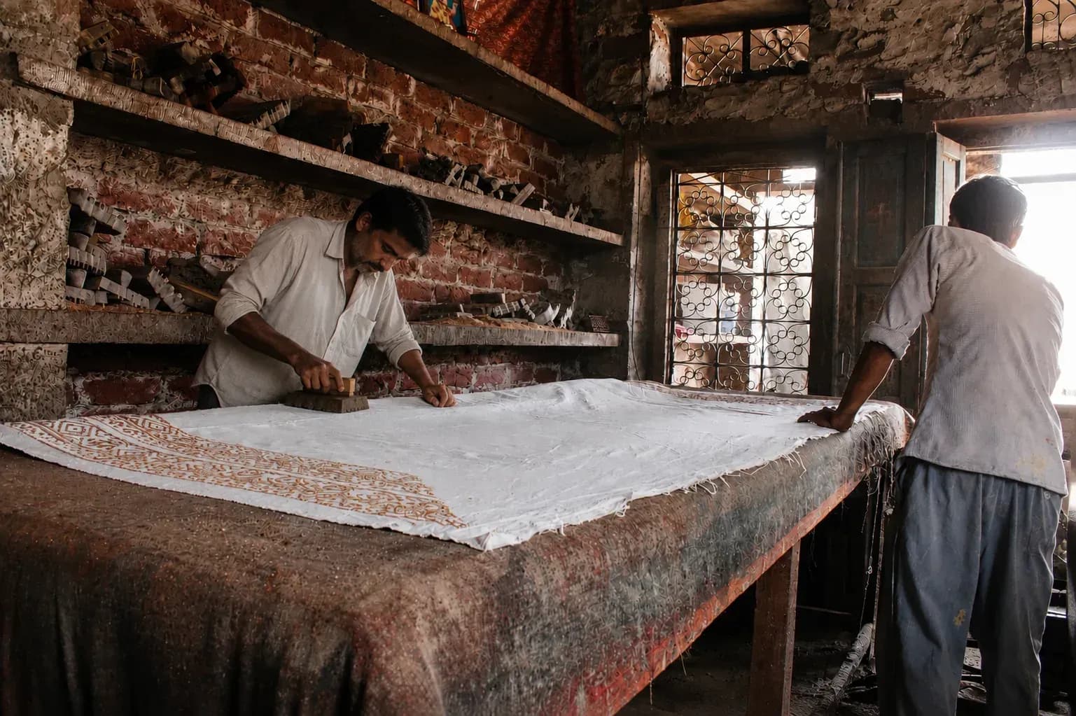 An artisan hand-pressing a carved teak block onto block-printed cloth.